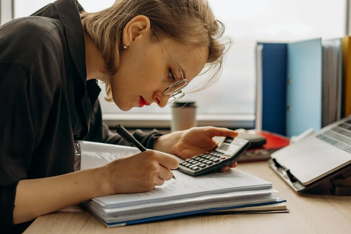 Small business owner checking a regulator register on a laptop with a calculator nearby